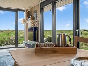 Ein modernes Interieur mit großen Fenstern, einem Holztisch und einer Kaffeestation.