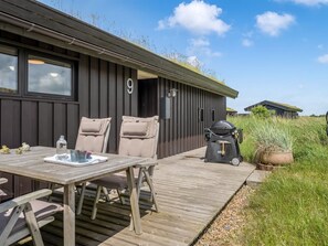 A wooden deck with a table and chairs, a barbecue grill, and a building with a number '9' on the wall. - "Beatrice" - 350m from the sea by Interhome (Pandrup)