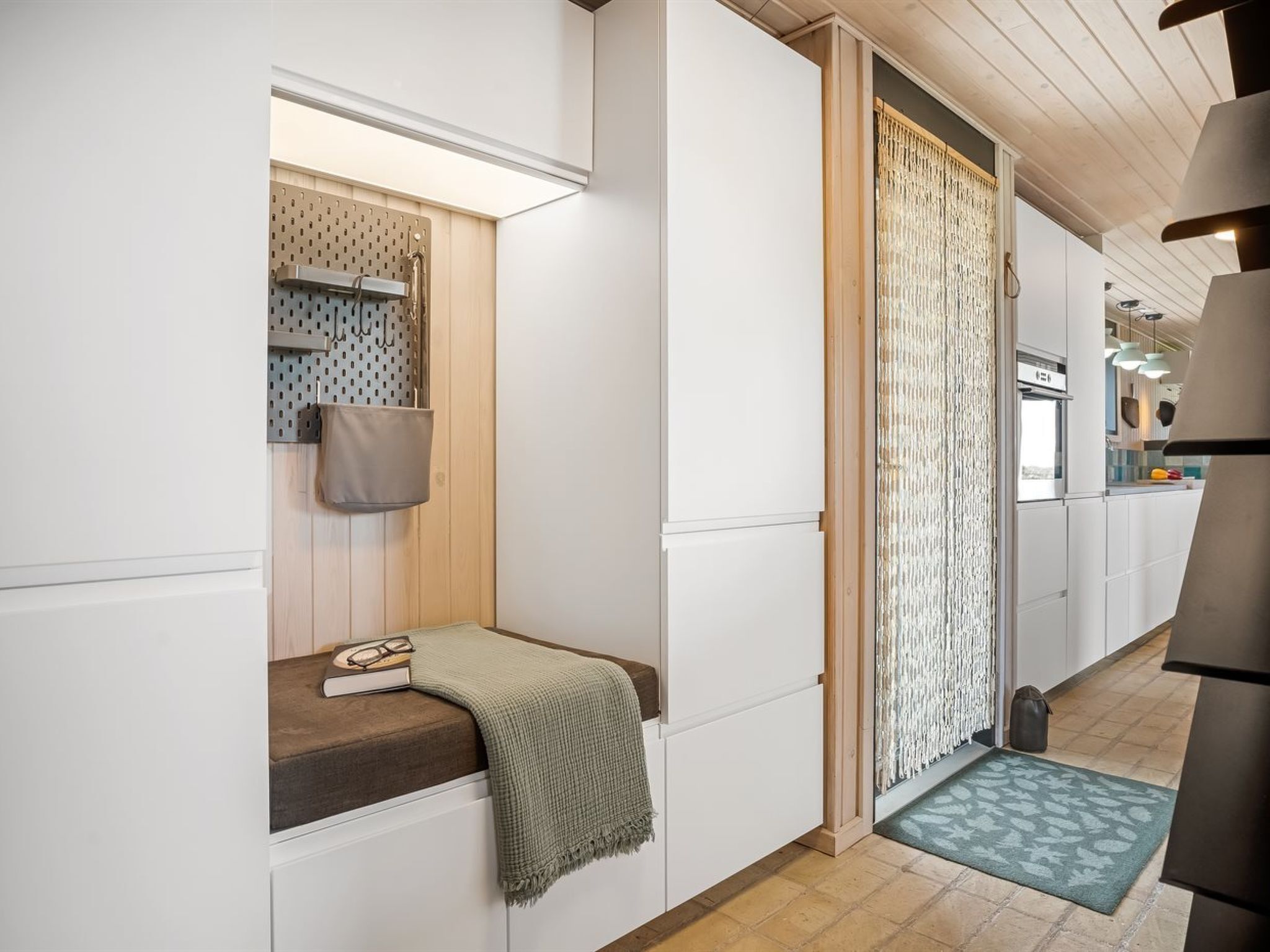 A hallway with a bench, a door with a patterned curtain, and a kitchen area in the background.