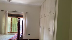 A bedroom with a bed, a window with curtains, a wardrobe, and a chandelier. - Peaceful 4-bedroom house in Fort Portal perfect for relaxing stays (Fort Portal)