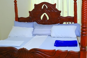 Een bed met een houten hoofdbord, wit beddengoed en een blauw object op het bed.