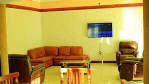 A living room with a brown leather sofa, a wooden chair, a recliner, and a flat-screen TV mounted on the wall. - Peaceful 4-bedroom house in Fort Portal perfect for relaxing stays (Fort Portal)