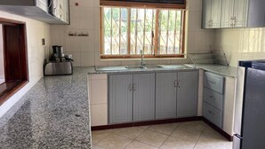 A kitchen with granite countertops, grey cabinets, a window with bars, a sink, and a refrigerator. - Peaceful 4-bedroom house in Fort Portal perfect for relaxing stays (Fort Portal)