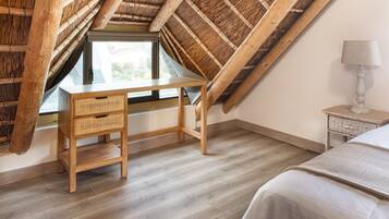 A room with a sloped ceiling, a wooden desk with drawers, a bedside table, and a lamp.