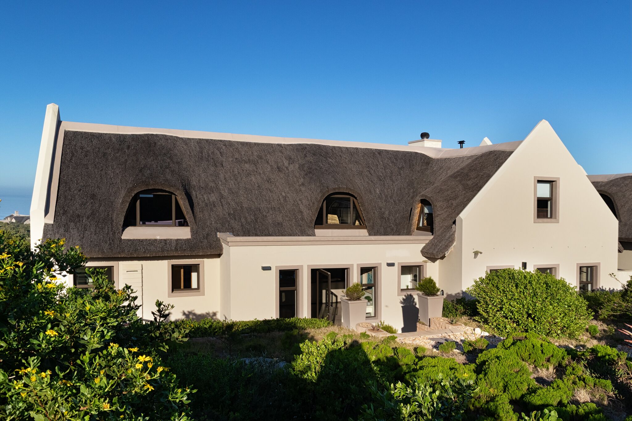 A modern house with a unique thatched roof, multiple entry points, and a well-maintained garden.
