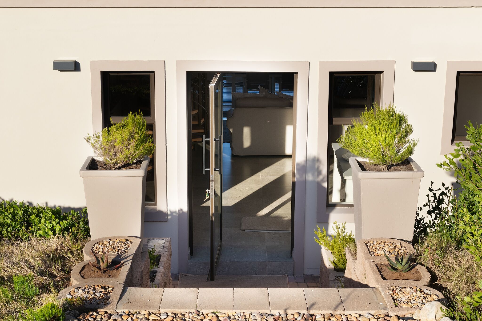 A building entrance with a glass door, potted plants, and a pathway leading to the door.