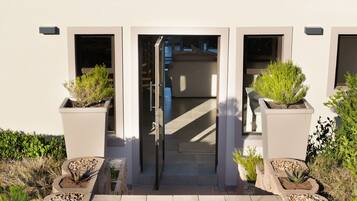 A building entrance with a glass door, potted plants, and a pathway leading to the door.