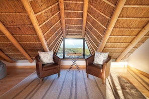 Una habitación con techo de madera alto, dos sillones de cuero con almohadones y una mesa, además de vistas a través de una ventana.