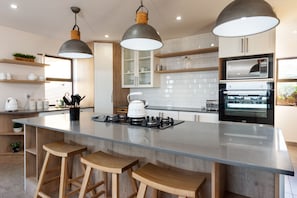 A modern kitchen with a central island, wooden stools, pendant lighting, and built-in cabinetry. - Bayview Bliss Springerbaai  (Mossel Bay)