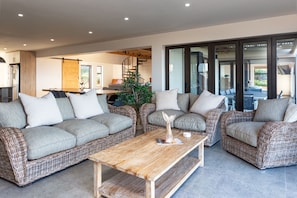 A modern living room with wicker furniture, a wooden coffee table, and a staircase leading to an upper level. - Bayview Bliss Springerbaai  (Mossel Bay)