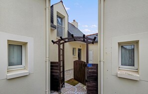 A narrow alleyway between two buildings with a wooden gate, a tiled floor, and a clear sky. - Maison près de la mer (la Turballe)