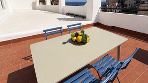 Una terrazza sul tetto con un tavolo, sedie blu e una ciotola di frutta.