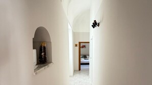 Un corridoio stretto con pareti bianche, pavimento piastrellato e un piccolo angolo con un vaso decorativo.