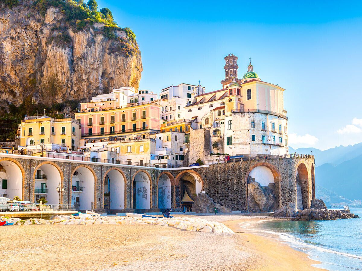 A coastal town with a prominent church featuring a bell tower and arched walkways.