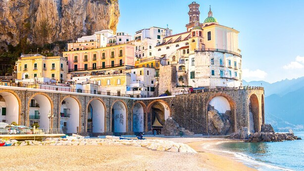 Una cittadina costiera con una chiesa in evidenza, un campanile e porticati ad arco.