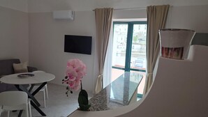 Una camera moderna con TV a schermo piatto, un tavolo da pranzo con sedie, un balcone vista edifici e un'orchidea in vaso.