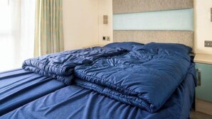 A bed with a blue duvet, a headboard with a light wood panel, and a window with curtains. - Holiday Home in Otterlo With Terrace (Otterlo)