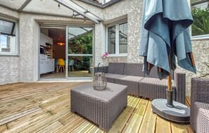 Eine überdachte Terrasse mit Korbmöbeln, einem Tisch und einem Grill.