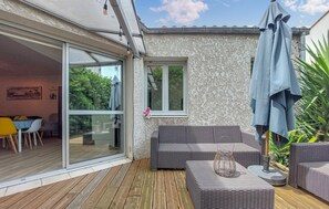 Eine Terrasse mit Korbmöbeln, eine Glastür zu einem Essbereich und ein kleines Fenster.