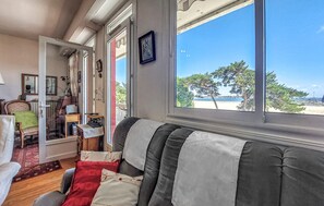 Ein Zimmer mit Blick auf den Strand, eine Sitzecke mit Sofa, Sessel und einem Tisch mit Lampe.