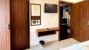 Una habitación de hotel con cama, televisión, aire acondicionado, puerta de madera y una pequeña repisa.