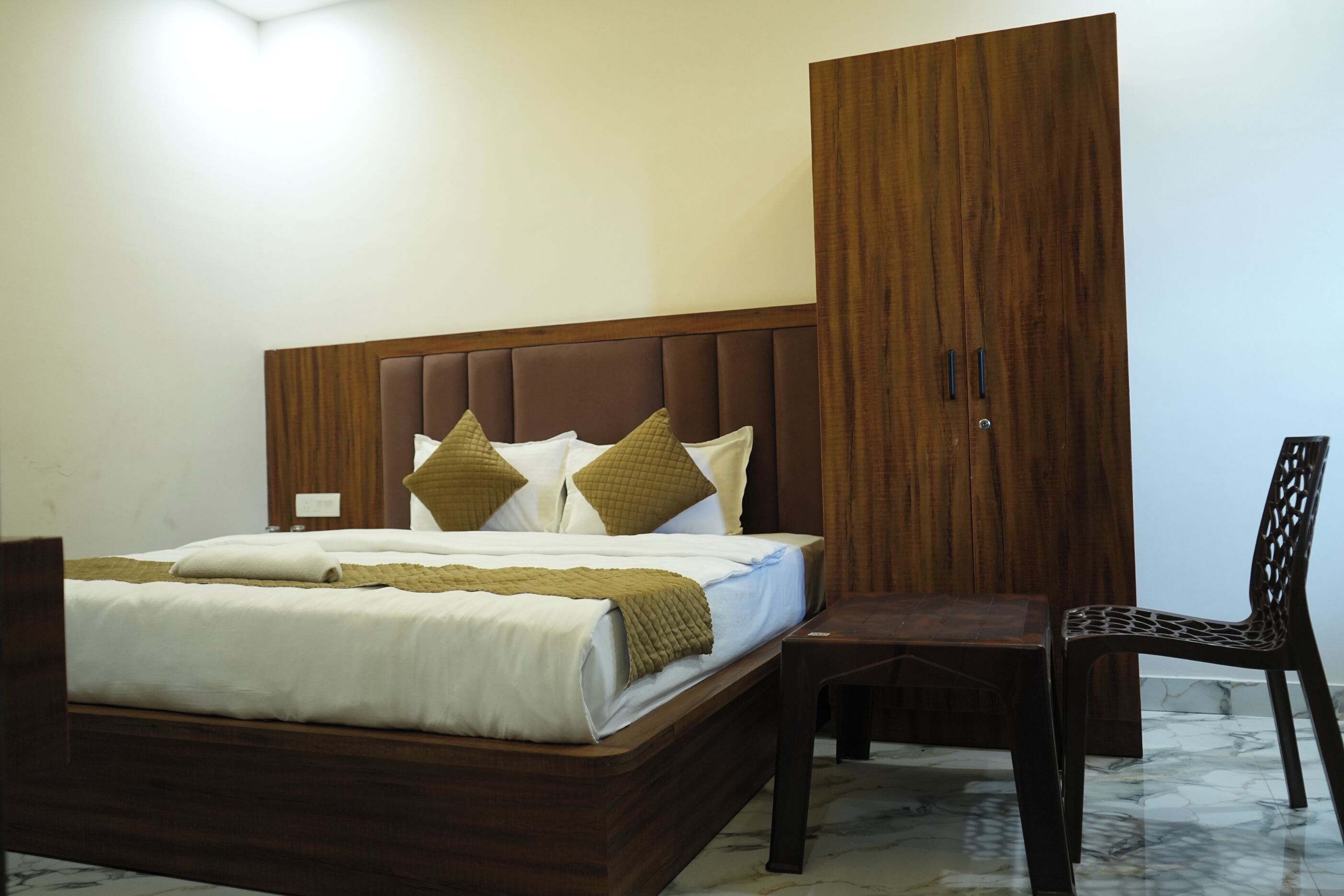 A bedroom with a bed, a wooden wardrobe, a desk, and a chair.