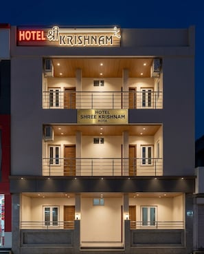 Un hotel de varios pisos con balcones, un letrero que indica 'HOTEL KRISHNAM' y otro letrero que dice 'HOTEL SHREE KRISHNAM'.