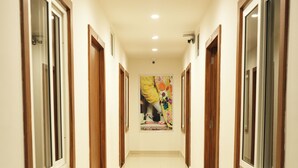 Un largo pasillo bien iluminado, con puertas y ventanas de madera a ambos lados, que conduce a una habitación con un cartel llamativo en la pared.