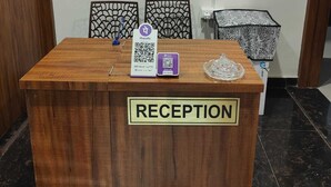 Una mesa de recepción con un cartel, un teléfono, un código QR y un objeto decorativo.