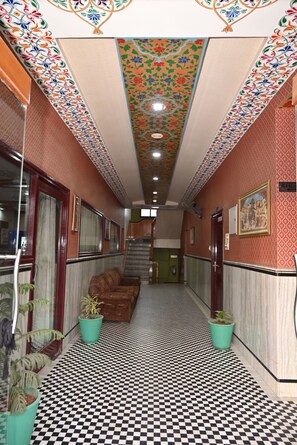 Un corridoio d'hotel con pareti decorate, pavimento a scacchi e piante in vaso.
