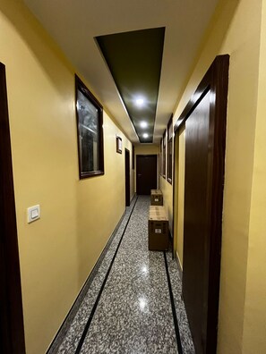 Un corridoio con pavimento piastrellato, porte in legno e quadri appesi alle pareti.