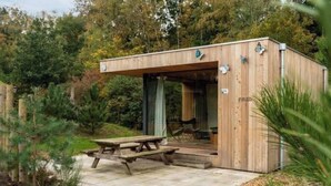 A wooden cabin with a covered porch, a picnic table, and a chair. - Holiday Home in Otterlo With Terrace (Otterlo)