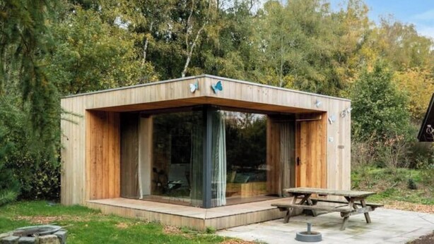 A modern wooden cabin with large glass windows, a picnic table, and a stone fire pit. - Holiday Home in Otterlo With Terrace (Otterlo)