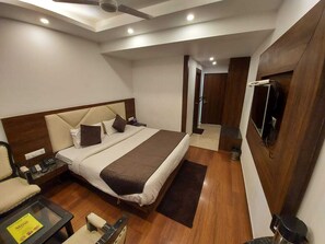 Een moderne hotelkamer met een groot bed, een aan de muur bevestigde televisie, een bureau met een stoel en een klein tafeltje met een menukaart.