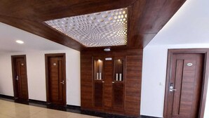 Un pasillo con tres puertas de madera, un techo con una lámpara de diseño geométrico y un suelo de baldosas.
