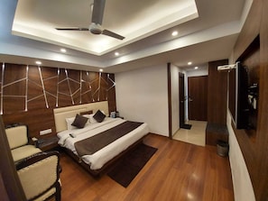 Ein modernes Hotelzimmer mit Bett, Nachttischen, einem Sessel, Deckenventilator und Fernseher.