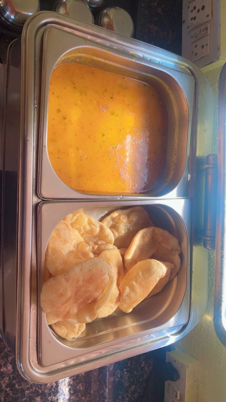 A stainless steel food container with a curry and bread.