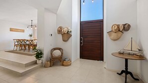 A modern interior with a dining area, wicker furniture, a wooden door, and wall-mounted hats. - Spacious Coastal Escape - Steps to Beach (Moffat Beach)
