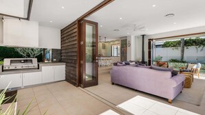 A modern kitchen with a built-in grill, a sliding glass door leading to a living area with a sofa and a dining table. - Spacious Coastal Escape - Steps to Beach (Moffat Beach)