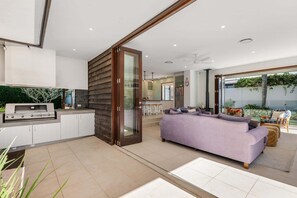 Eine moderne Küche mit integriertem Grill, eine Schiebetür zu einem Wohnbereich mit Sofa und Esstisch.