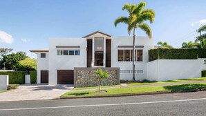 A modern two-story house with a stone facade, a garage, and a well-maintained lawn. - Spacious Coastal Escape - Steps to Beach (Moffat Beach)