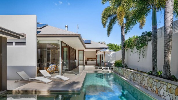 A modern house with a swimming pool, glass doors, and a stone wall. - Spacious Coastal Escape - Steps to Beach (Moffat Beach)