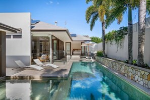 Une maison moderne dotée d’une piscine, de portes vitrées et d’un mur en pierre.