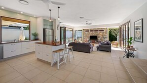 A modern kitchen with a central island, a dining area with a sofa, and a TV in the living room. - Spacious Coastal Escape - Steps to Beach (Moffat Beach)