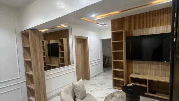 A modern living room with a sectional sofa, built-in shelving, a flat-screen TV, and a marble floor. - Glover Apartments (Lagos)