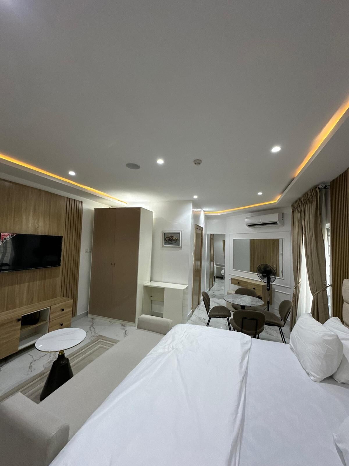 A hotel room with a bed, a TV, a desk, a chair, a mirror, and an air conditioning unit.