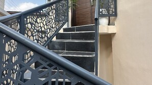 A staircase with a geometric metal railing, a beige wall, and a door with a potted plant beside it. - Glover Apartments (Lagos)