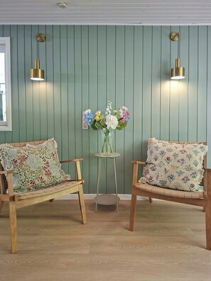 Ein Zimmer mit zwei Holzstühlen, einem kleinen Tisch mit Blumenvase und zwei Wandleuchten.