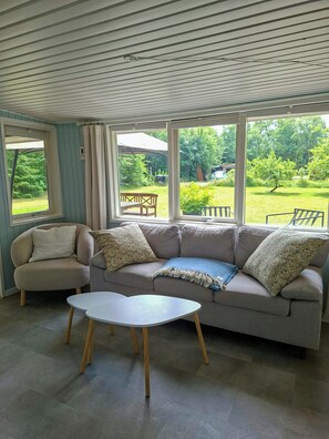 Ein Wohnzimmer mit einer Couch, einem kleinen Tisch und großen Fenstern mit Blick auf einen Garten.