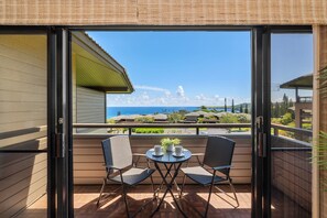 A balcony with two chairs and a table, a view of the ocean, and a building in the background. - Two-Story Ocean View Retreat Steps from Pool & Beaches -KRV 915 (Lahaina)